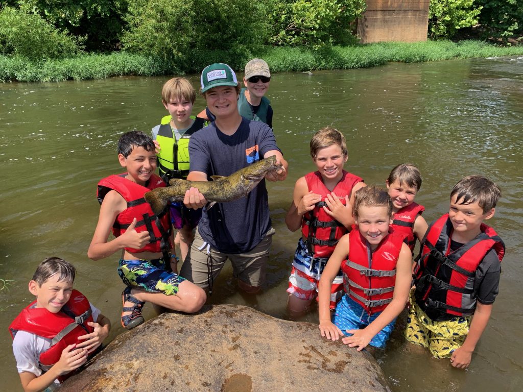 Campers standing in the river holding up the fish they caught